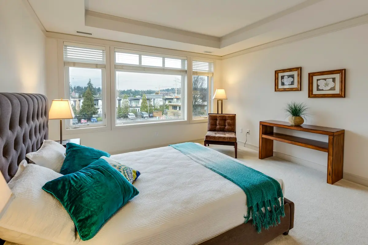 A bright bedroom with a made bed and a view of the city